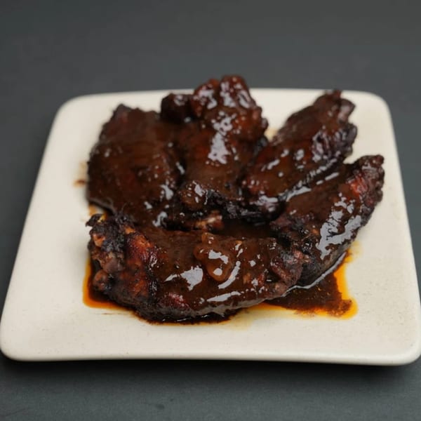 A plate of dark, glossy Jamaican jerk chicken wings covered in a rich sauce.