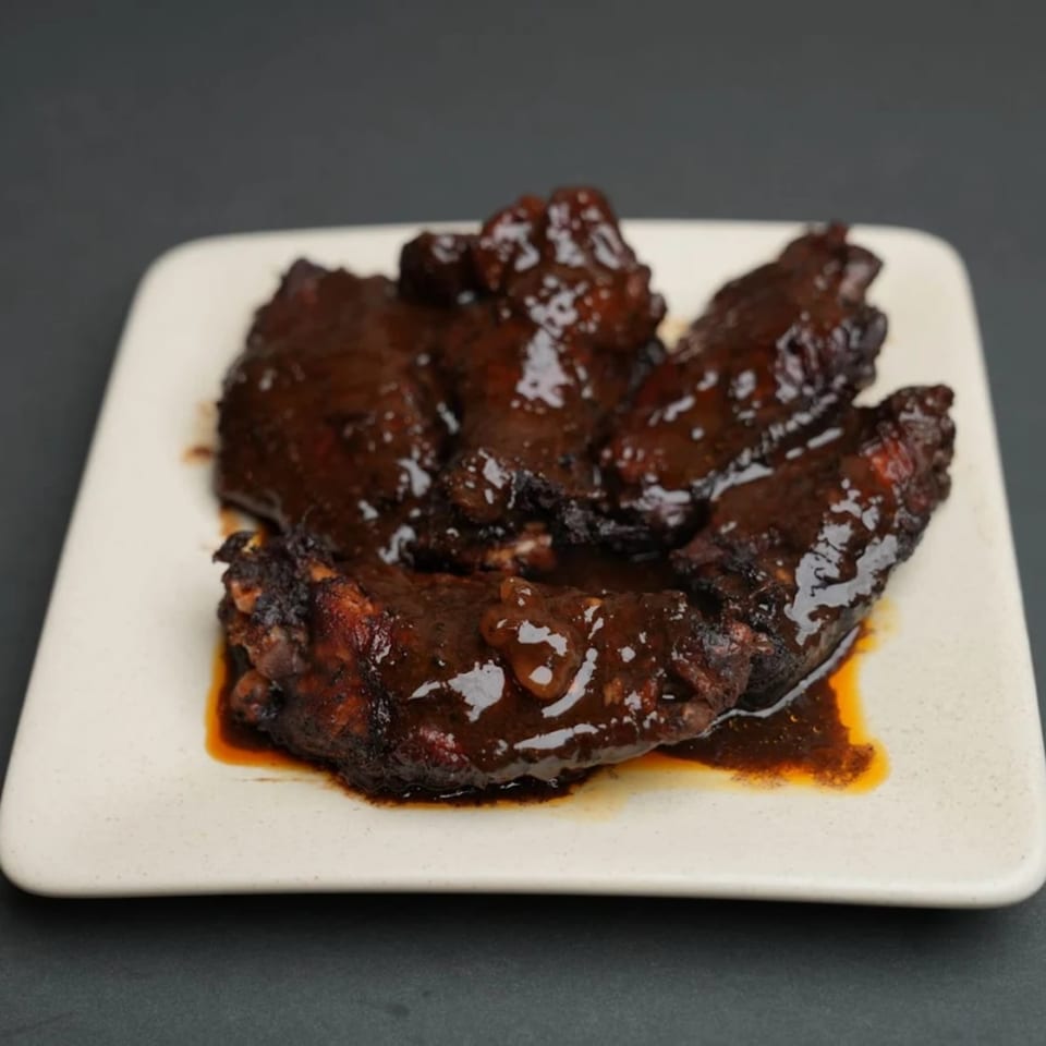 A plate of dark, glossy Jamaican jerk chicken wings covered in a rich sauce.