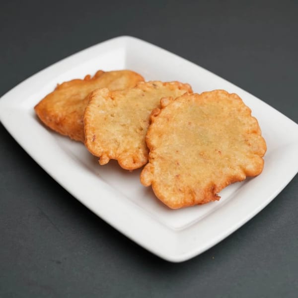 Three golden-brown Jamaican festival dumplings, with ruffled edges, arranged on a white rectangular plate.