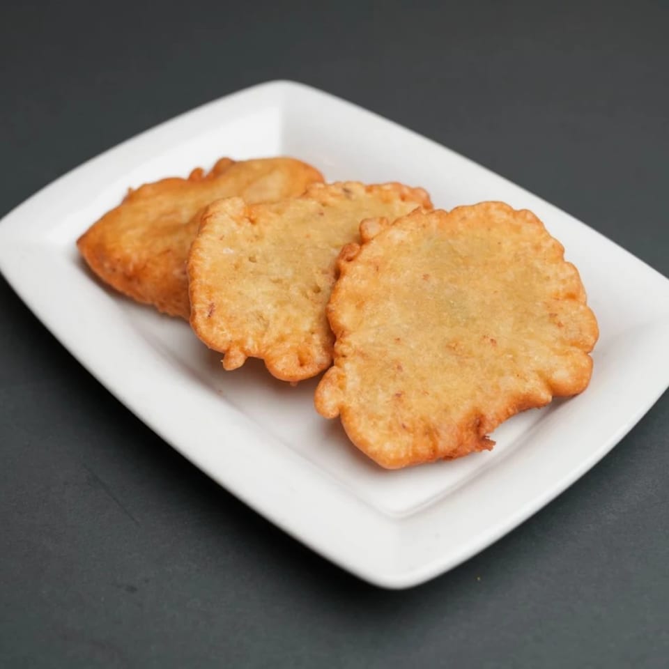 Three golden-brown Jamaican festival dumplings, with ruffled edges, arranged on a white rectangular plate.