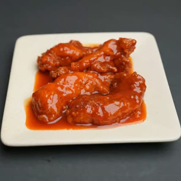 A white rectangular plate holds several pieces of Jamaican jerk chicken wings coated in a vibrant red sauce.