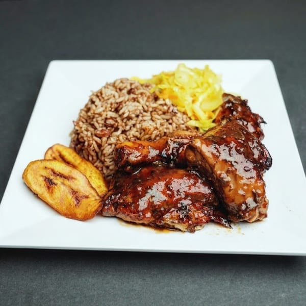 A plate of Jamaican jerk chicken, rice and peas, fried plantains, and yellow cabbage.